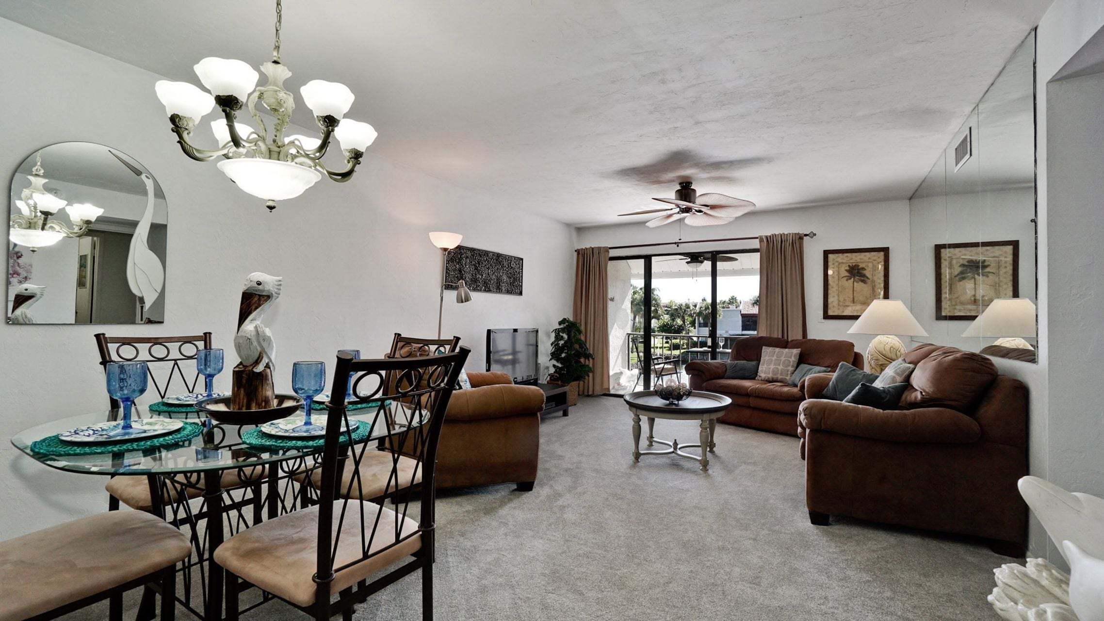 A spacious living room with a dining area, a ceiling fan, and a large window offering a view.