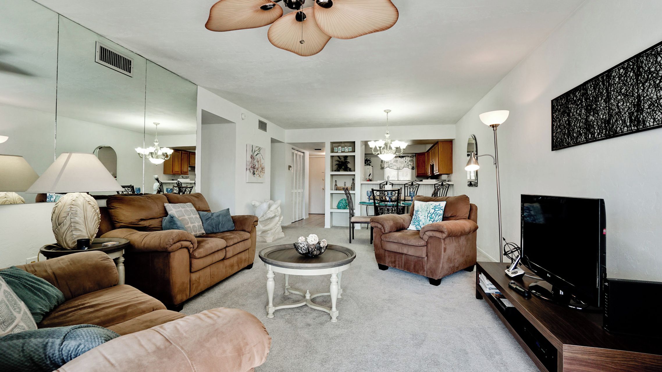 A living room with a sofa, armchairs, a coffee table, and a TV. There is a dining area in the background with a table and chairs.