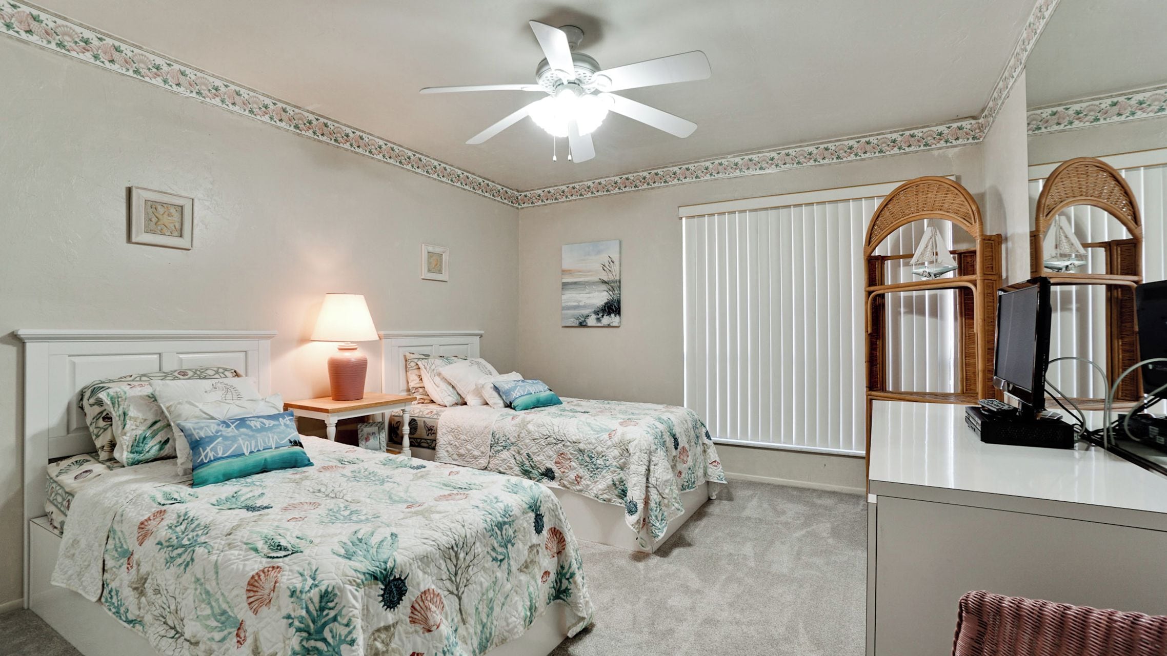 A bedroom with two beds, a ceiling fan, a desk with a computer, and a window with blinds.