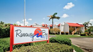 A sign for Runaway Bay Condominium with a red roof and palm trees in the background. - Runaway Bay 213 - 1845191 (Bradenton Beach)