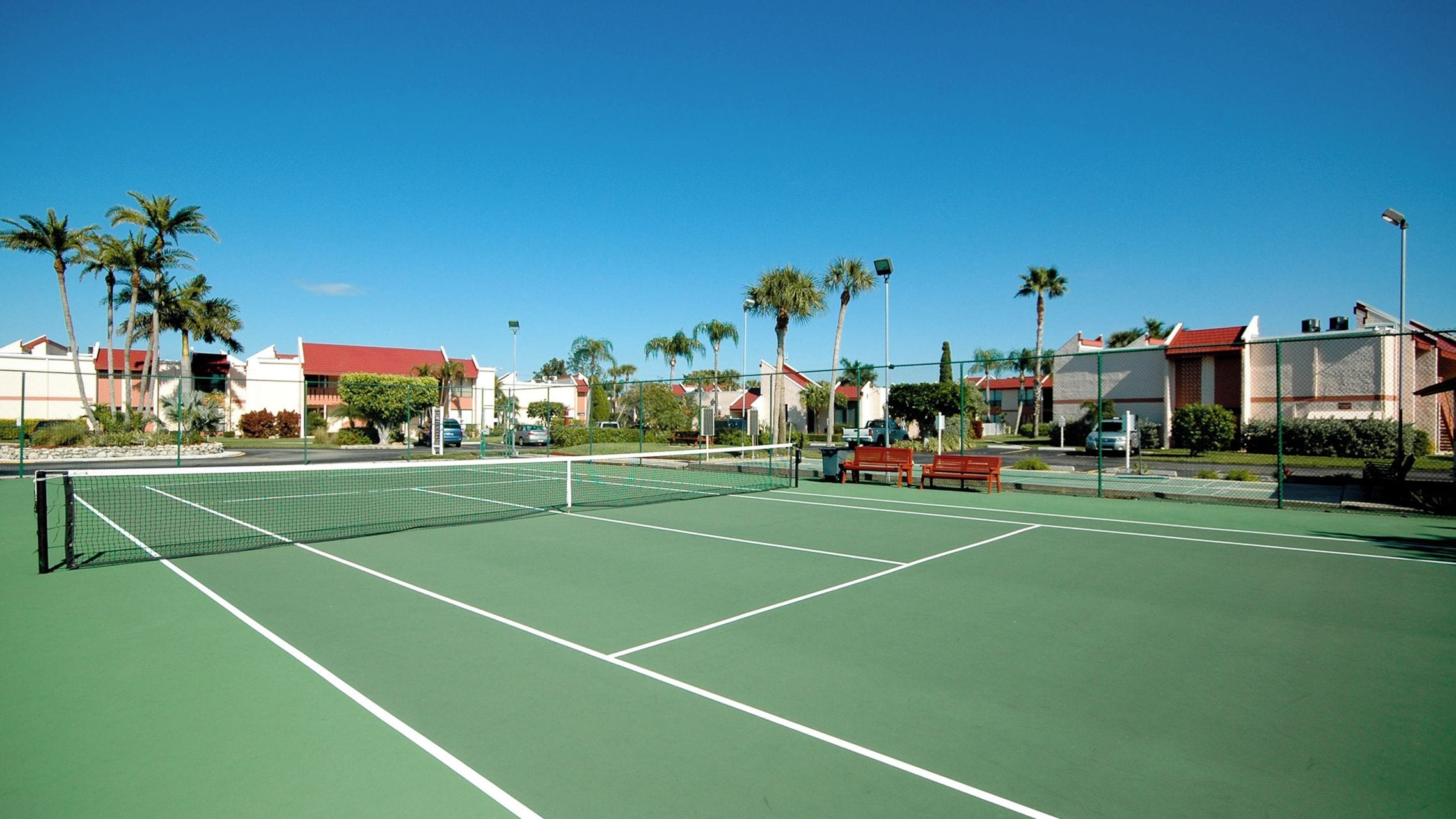 Una cancha de tenis con una red, rodeada de palmeras y edificios.
