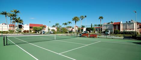 Una cancha de tenis con una red, rodeada de palmeras y edificios.