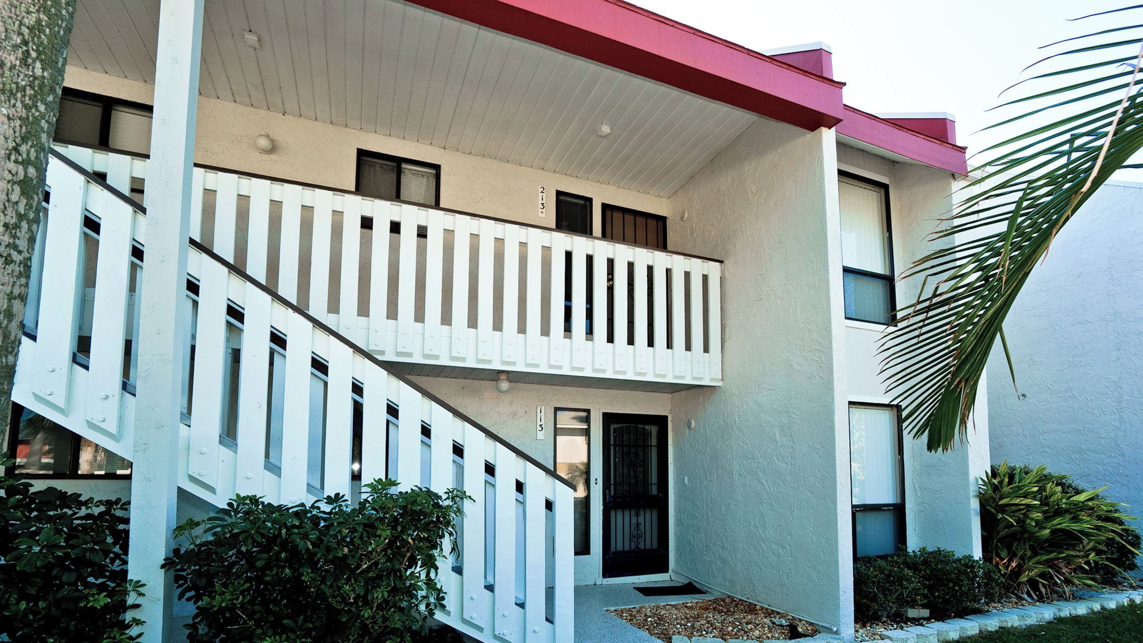 A two-story building with a white exterior, a red roof, and a balcony on the second floor.