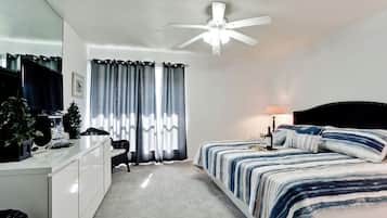 A bedroom with a bed, a desk, a chair, a ceiling fan, and a TV.