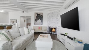 Een moderne woonkamer met een witte bank, een salontafel, een open haard en een wandtelevisie.