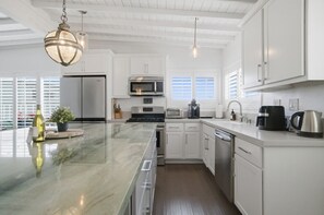 Une cuisine moderne avec des meubles blancs, un grand îlot central, des appareils en acier inoxydable et des luminaires suspendus.