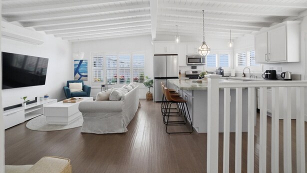 Een modern interieur met een zithoek, keuken en eethoek, met witte kasten, een flatscreen televisie en een groot raam.