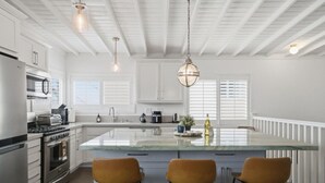 Een keuken met witte kasten, een centraal eiland met krukken, een fornuis en een hangende lamp.