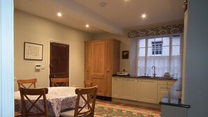 A compact kitchen with wooden cabinets, a dining table with chairs, and a patterned rug. - Charming 3 bedroom house in the heart of Ludlow (Ludlow)