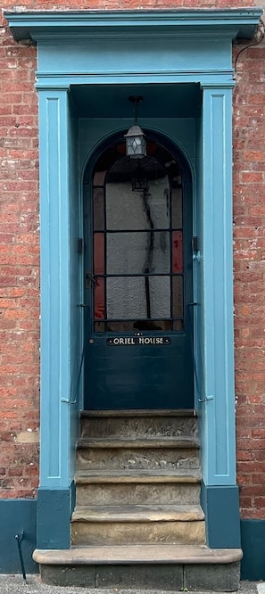 A blue door with a sign reading 'ORIEL HOUSE' above a set of stone steps leading to a brick building. - Charming 3 bedroom house in the heart of Ludlow (Ludlow)