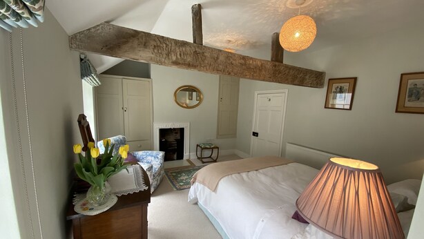 A bedroom with a bed, a bedside lamp, a dresser, a mirror, a fireplace, and a ceiling with exposed beams. - Charming 3 bedroom house in the heart of Ludlow (Ludlow)