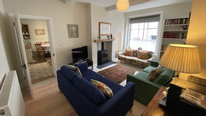 A living room with a blue sofa, a green armchair, a fireplace, a bookshelf, and a dining area in the background. - Charming 3 bedroom house in the heart of Ludlow (Ludlow)