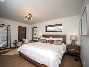 Ein Schlafzimmer mit einem großen Bett, Nachttischen, einem Spiegel und einer Deckenleuchte.