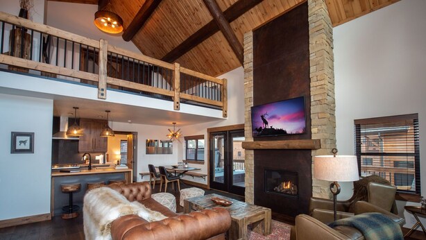 Un amplio salón con chimenea, muebles de cuero y un techo alto con vigas a la vista.