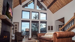 Un amplio salón con chimenea, muebles de cuero, ventanas grandes y techo de madera.