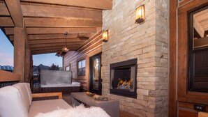 A cozy outdoor seating area with a stone fireplace, wooden furniture, and a view of the mountains. - Rocky Mountain Escape - Steps to Lake Estes, Jacuzzi, Close to Downtown Estes (Estes Park)