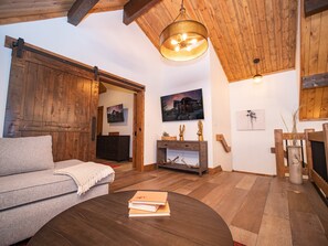 Un salon chaleureux avec un plafond en bois, un canapé, une table basse avec des livres, un meuble en bois et un tableau au mur.