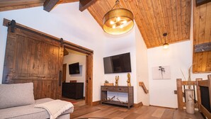 A cozy living room with a sofa, a coffee table with books, a wooden ceiling, a TV, and a fireplace. - Rocky Mountain Escape - Steps to Lake Estes, Jacuzzi, Close to Downtown Estes (Estes Park)