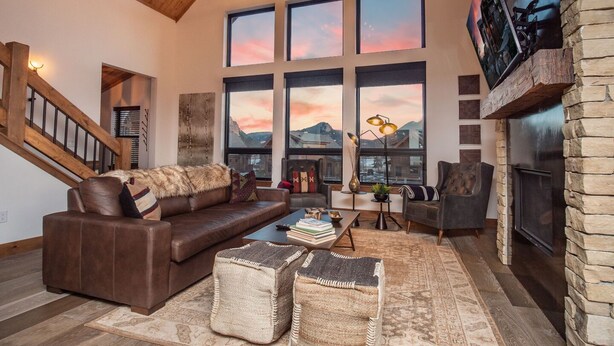 A spacious living room with a high ceiling, large windows, a fireplace, and a cozy seating area. - Rocky Mountain Escape - Steps to Lake Estes, Jacuzzi, Close to Downtown Estes (Estes Park)