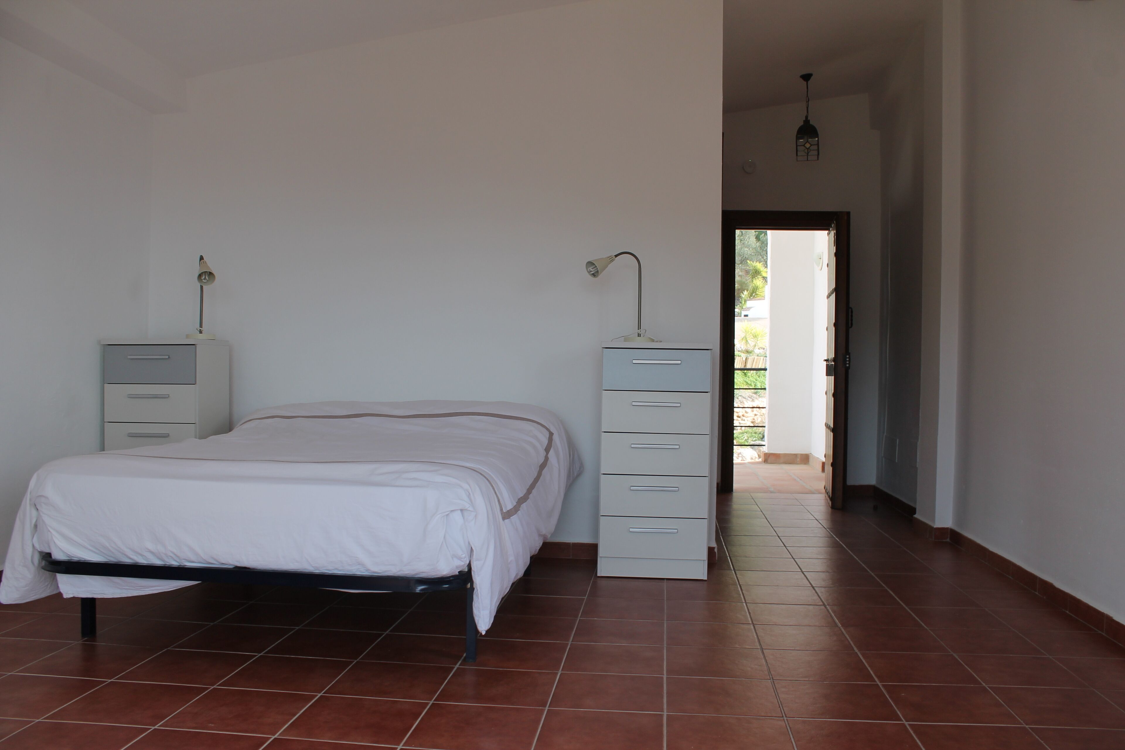 Een slaapkamer met een bed, nachtkastje, dressoir en lamp.