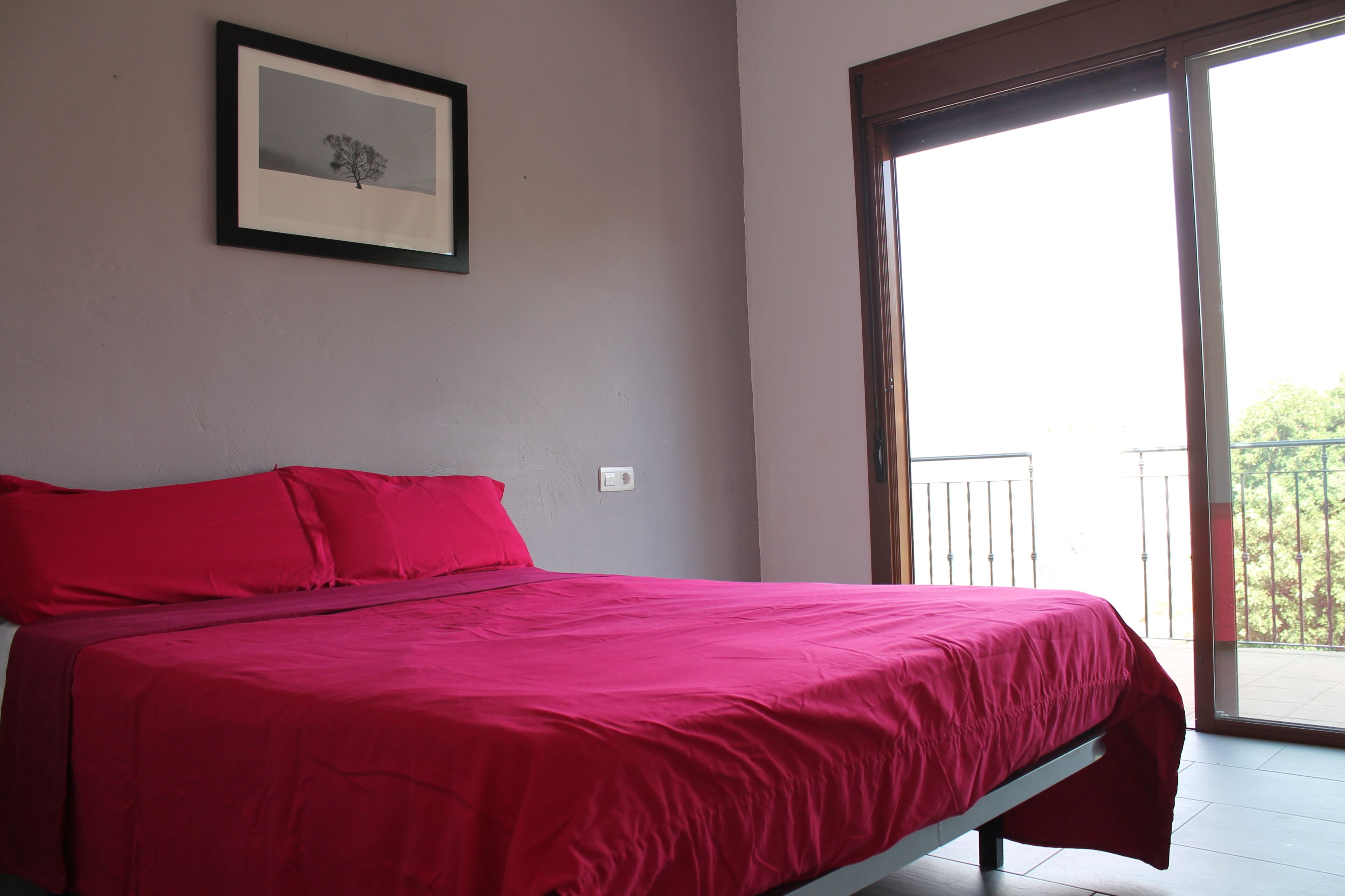 A bedroom with a bed, a framed picture on the wall, and a balcony.