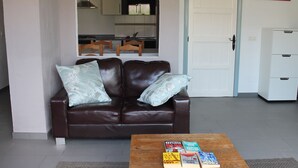 A living room with a brown leather sofa, two light blue pillows, and a wooden coffee table with books. - Casa Arts (Alcaucin)
