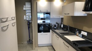 Una cocina moderna con armarios blancos, un horno Bosch, una placa de inducción negra y un lavamanos de acero inoxidable.