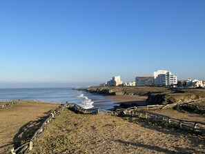 A coastal area with a sandy beach, rocky outcrops, and a wooden fence.