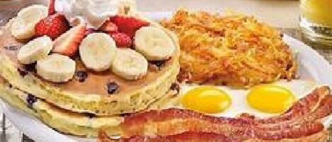A breakfast plate with pancakes topped with strawberries and bananas, hash browns, two eggs, and bacon.