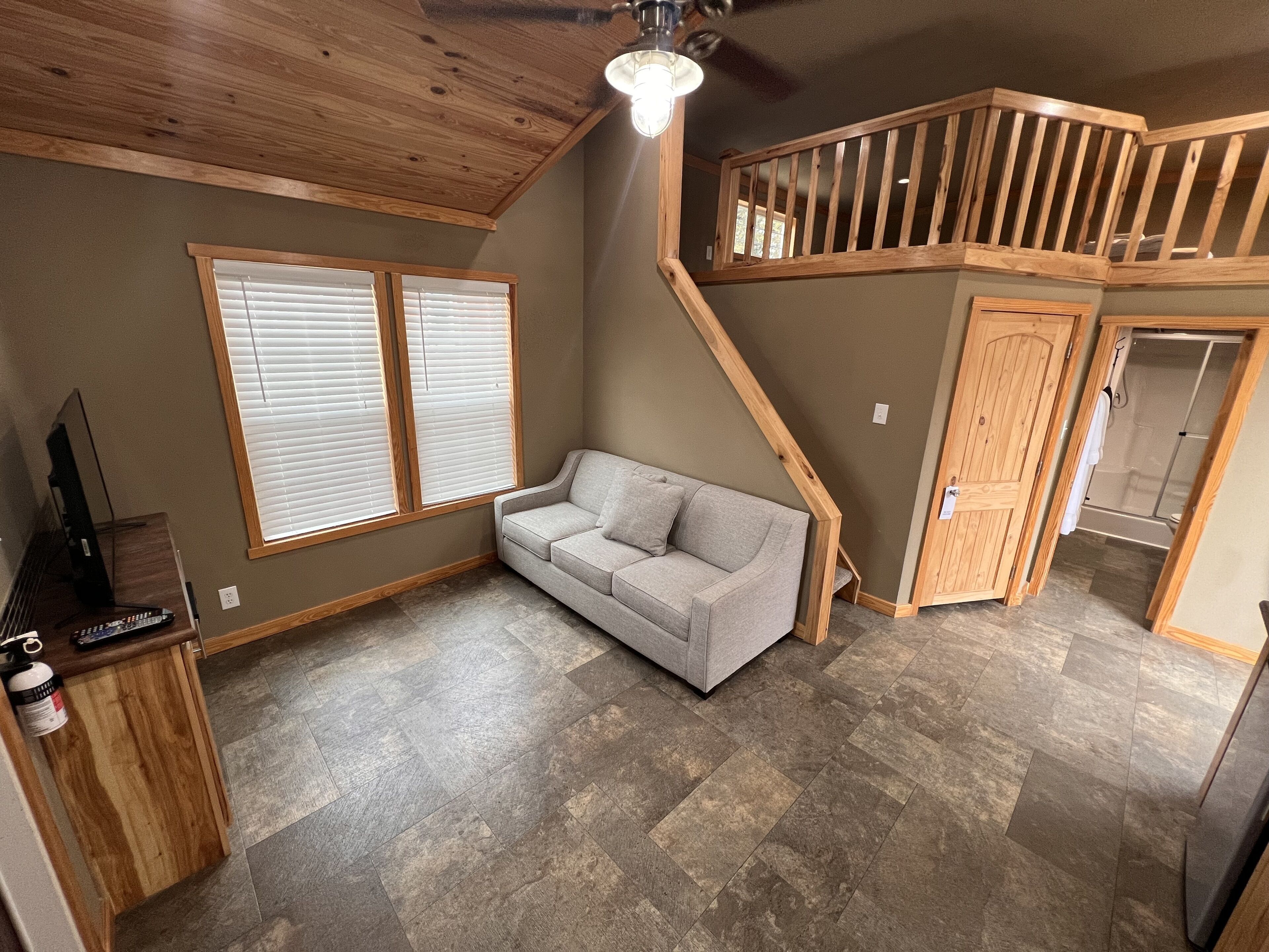 Amplia sala de estar con sofá gris, techo de madera y una escalera que conduce a un nivel superior.