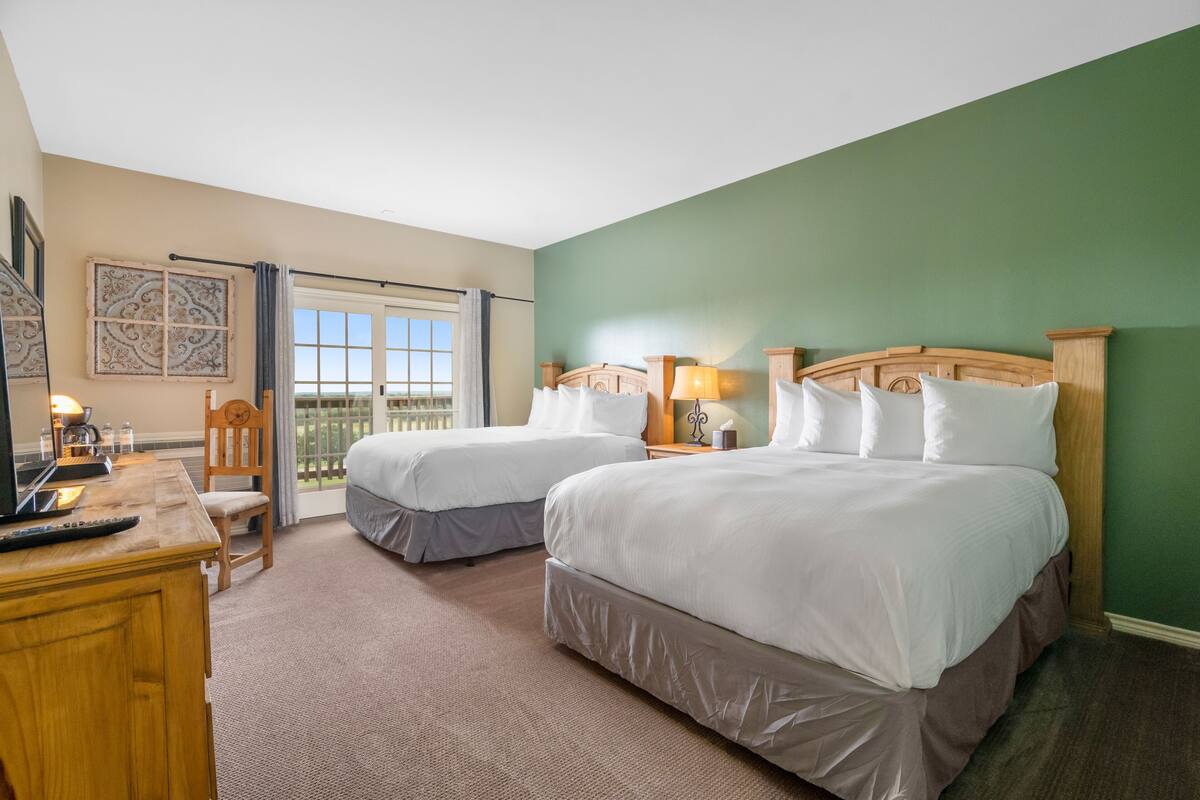 A hotel room with two beds, a desk with a computer, a chair, and a window with a view.