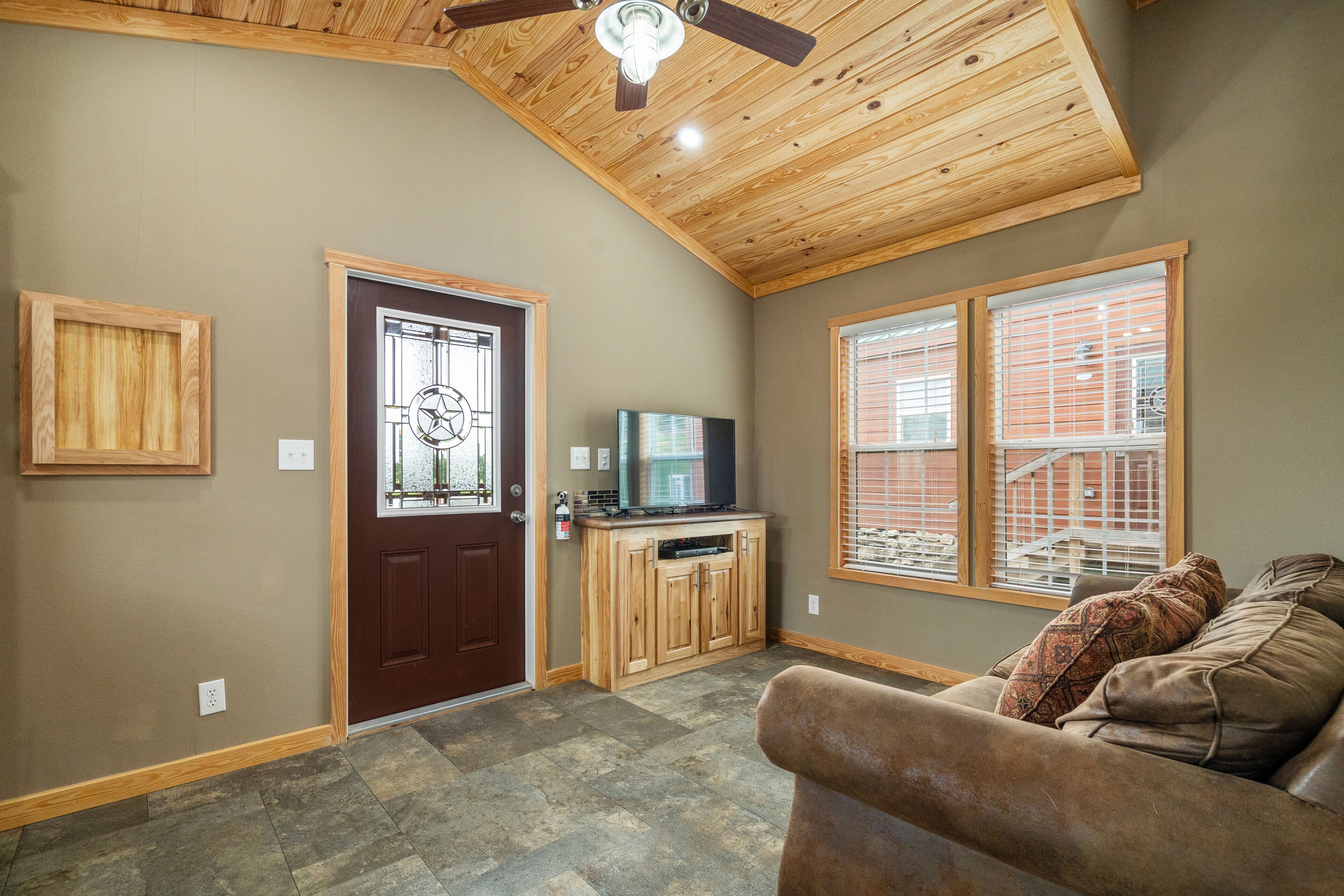 A living room with a brown leather couch, wooden ceiling, and a TV on a wooden cabinet.