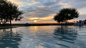 A swimming pool with a sunset view, surrounded by trees and lounge chairs.