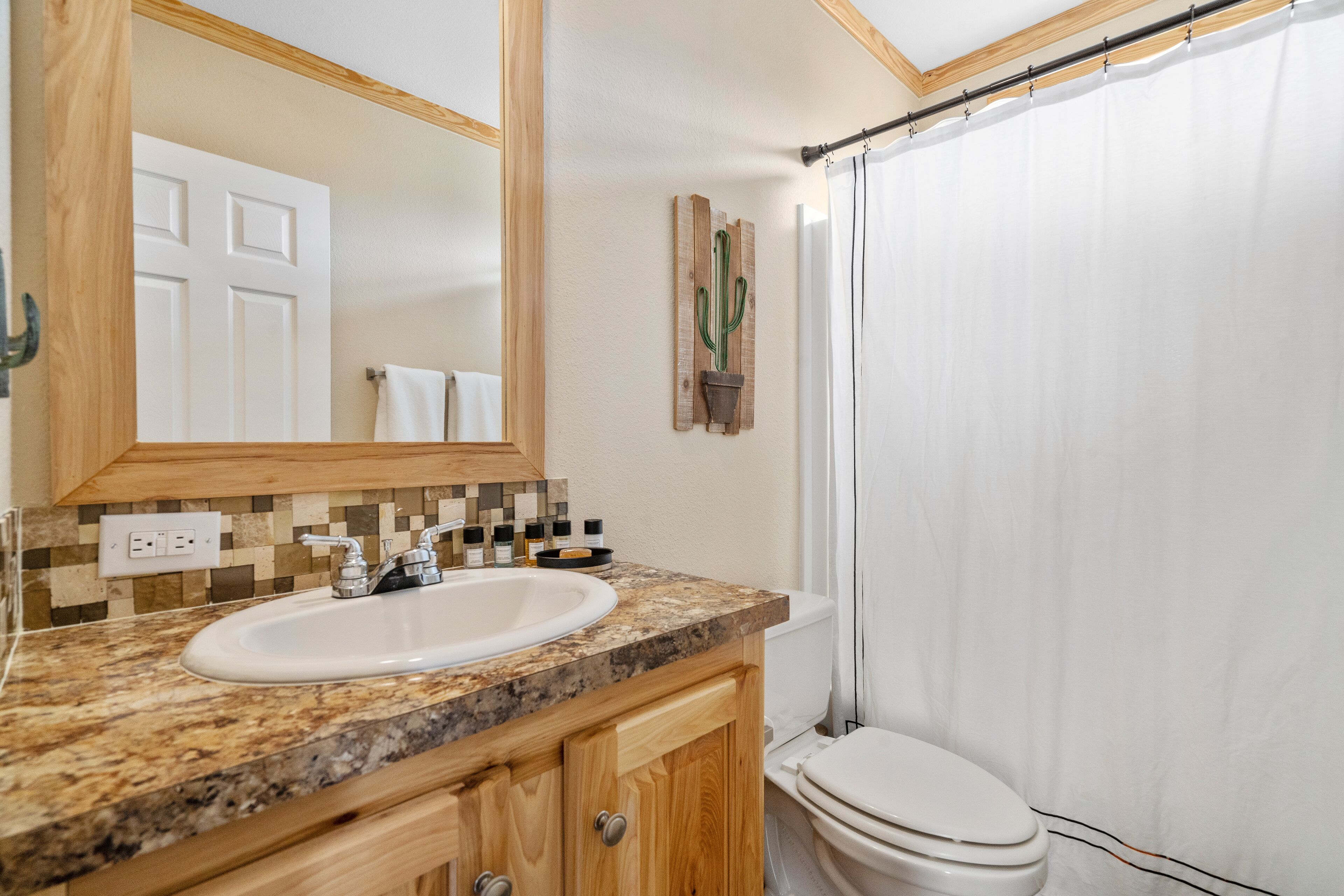 A bathroom with a wooden vanity, a sink, a mirror, a cactus decoration, and a shower curtain.