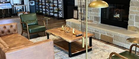 A spacious living area with a stone fireplace, green upholstered chairs, a wooden coffee table, and a modern floor lamp.