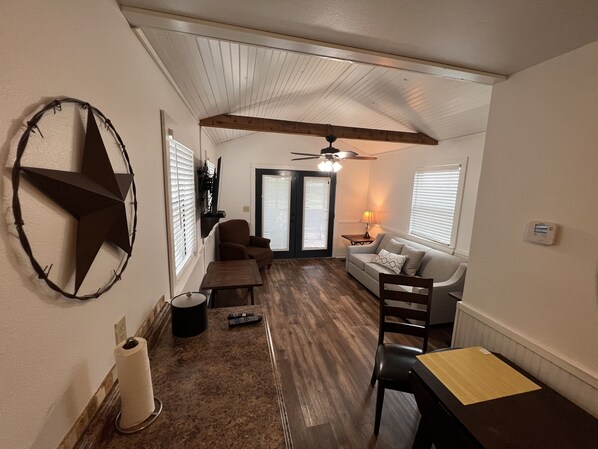 Un espacio habitable pequeño con ventilador de techo, decoración de pared con estrellas, sofá, mesa de comedor y televisor montado en la pared.