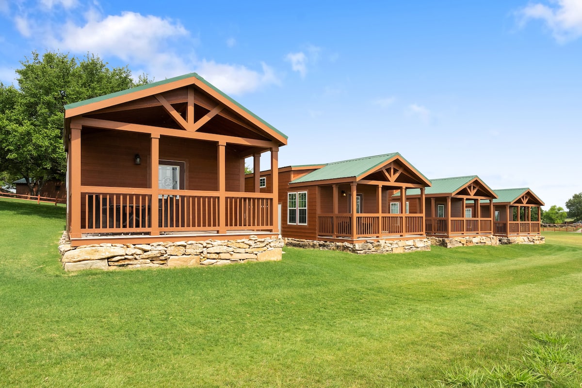 A row of wooden cabins with stone foundations, set on a well-maintained lawn.