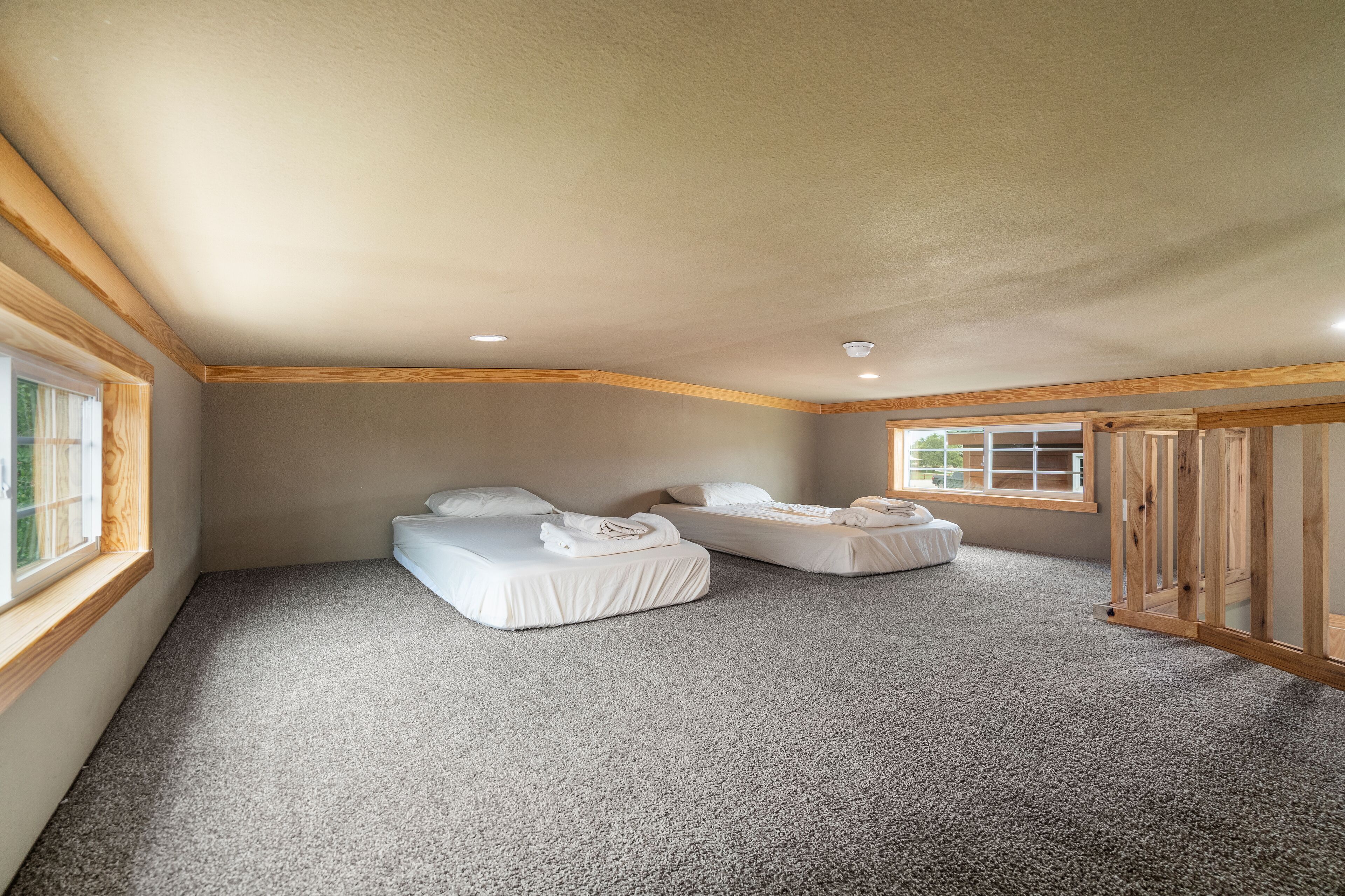 A bedroom with two beds, a carpeted floor, wooden beams, and a window.