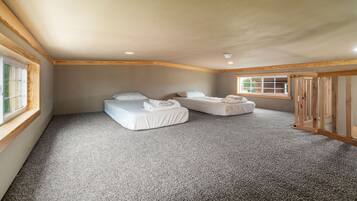A bedroom with two beds, a carpeted floor, wooden beams, and a window.