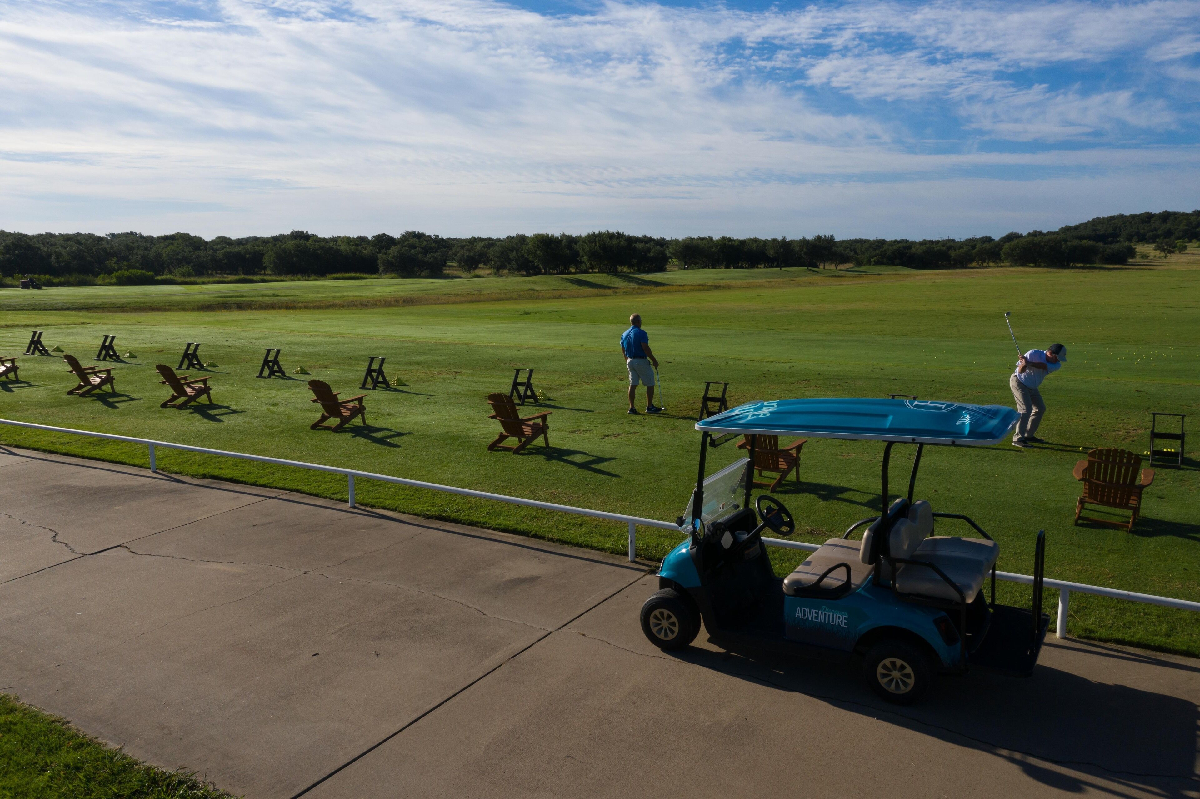 A golf course with a cart, chairs, and a person in a blue shirt.