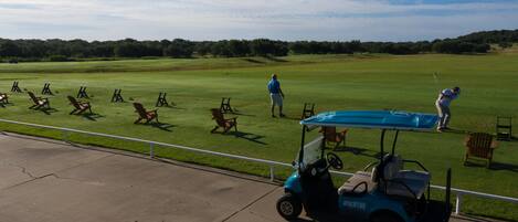 Een golfbaan met een golftrolley, stoelen en een persoon in een blauw shirt.