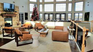 A spacious living room with a fireplace, comfortable seating, a large window with multiple panes, and a decorated Christmas tree.