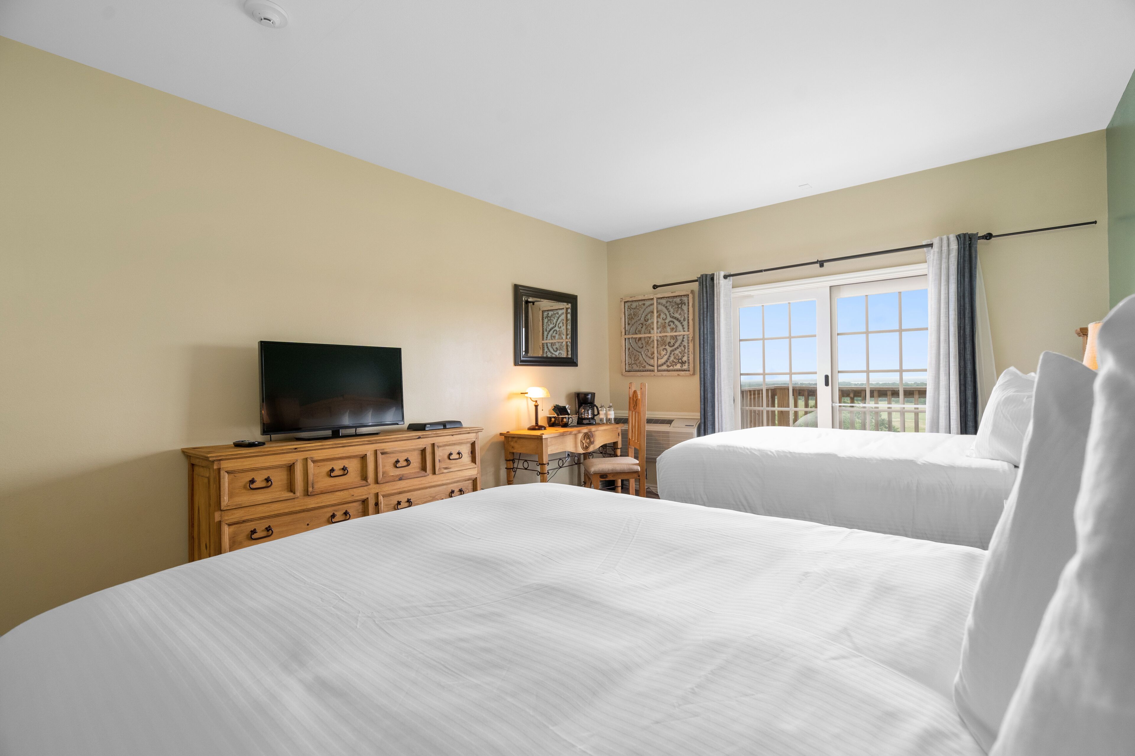 A hotel room with two beds, a TV, a desk with a lamp, and a window with curtains.