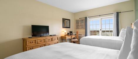 A hotel room with two beds, a TV, a desk with a lamp, and a window with curtains.