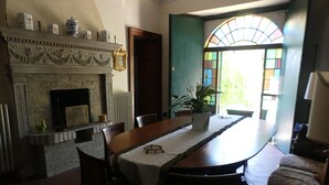 A dining room with a fireplace, a table set for four, and a view through a window. - Elegant house inside our period villa surrounded by centuries-old park (Marche)