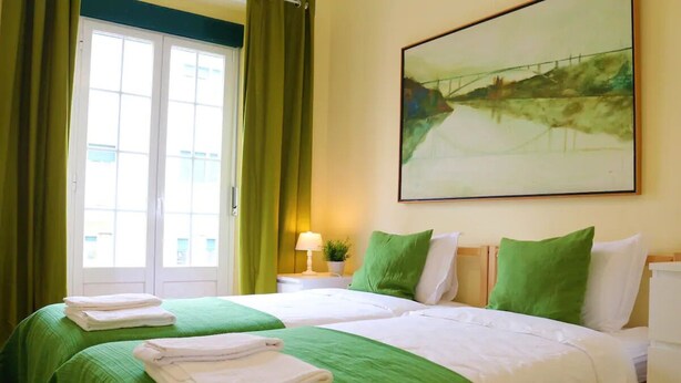 Habitación de hotel con dos camas, ropa de cama verde, un cuadro en la pared y vistas por la ventana.