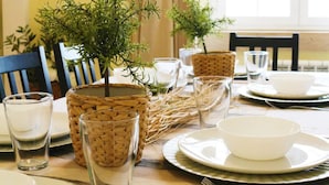 Una mesa de comedor dispuesta con platos, vasos y cubiertos, junto con cestas de mimbre y pequeñas macetas.