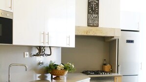 Una cocina moderna con armarios blancos, un lavamanos de acero inoxidable, una estufa a gas y un horno empotrado.