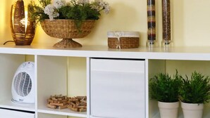 Una estantería con elementos decorativos, incluyendo un cuenco de mimbre con flores, un abanico y dos recipientes de vidrio.