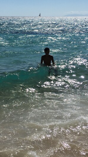 A person in the ocean with a sailboat in the distance. - Jasmin Penthouse Vacation Home (Quartu Sant'Elena)